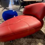 Rode fauteuil met unieke vorm, naast een blauwe poef, showroommodel met 30% korting, nu €3000,-.