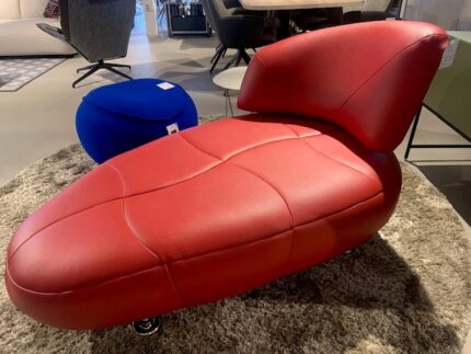 Rode fauteuil met unieke vorm, naast een blauwe poef, showroommodel met 30% korting, nu €3000,-.